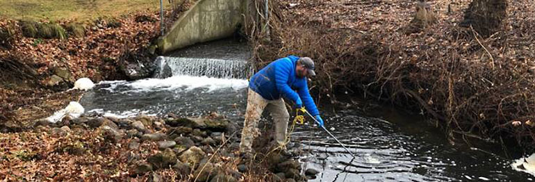 person collecting water sample from creek